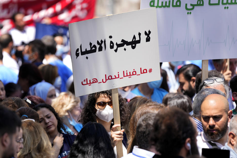 A medical worker holds an Arabic placard that reads: "No to doctors emigration, we cannot continue like this," as she protests with doctors the deteriorating economic conditions, outside the Central Bank, in Beirut, Lebanon, Thursday, May 26, 2022. The syndicates of doctors in Beirut and the North as well as the Syndicate of Private Hospital Owners declared a two-day general strike Thursday and Friday. (AP Photo/Hussein Malla)