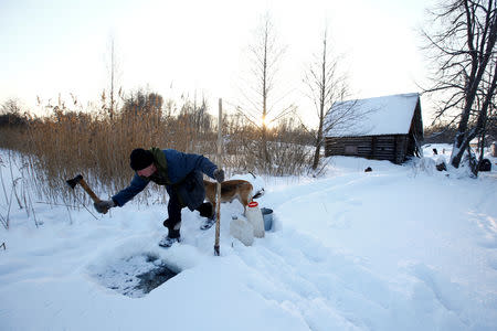 Yuri Baikov, 69, cuts a hole to take water from frozen river at his small farm situated in a forest near the village of Yukhovichi, Belarus, February 7, 2018. REUTERS/Vasily Fedosenko