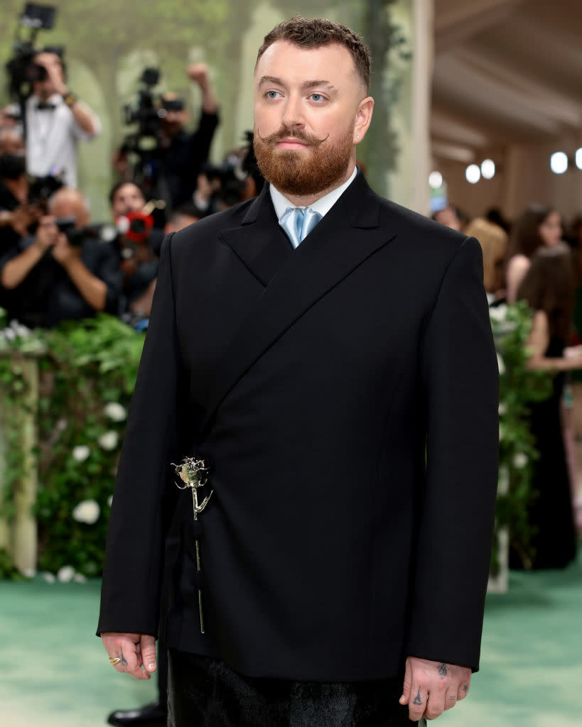 Sam wearing a suit with an asymmetrical jacket and silver rose on the red carpet