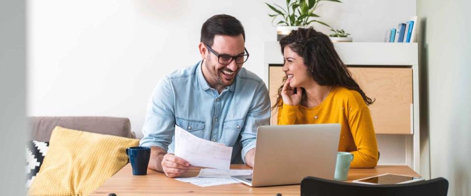 Smiling couple managing finances, reviewing their bank accounts using laptop computer and calculator at modern kitchen stock photo