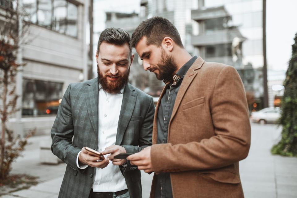 Two investors standing outdoors in a city look at something on a phone.