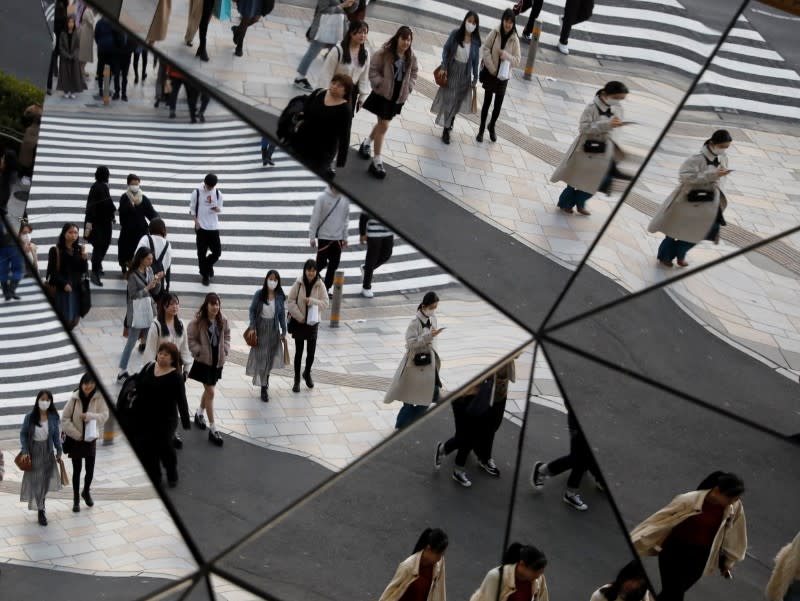 Passersby wearing protective face masks, following an outbreak of the coronavirus disease (COVID-19), are reflected in mirrors at a shopping center in Tokyo