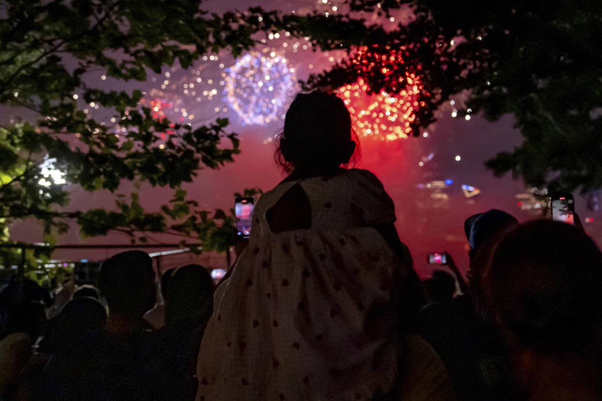 A girl sitting on someone's shoulders among a crowd of people in Hoboken, N.J., watches Macy's 4th of July Fireworks show.