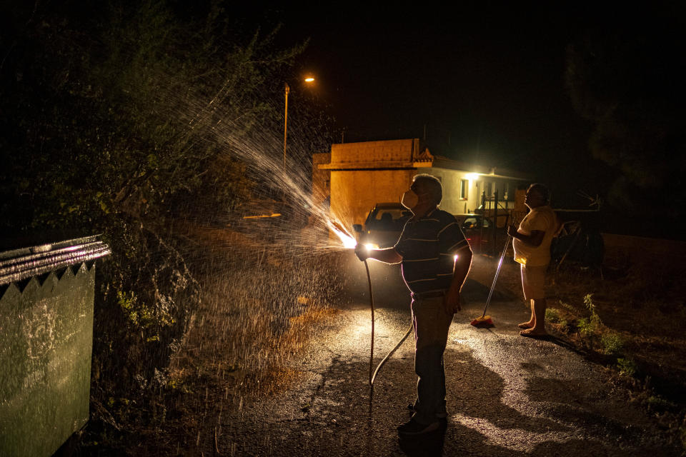 Local residents cool their houses with water to prevent it from flames as fire advances through the forest in La Orotava in Tenerife, Canary Islands, Spain on Saturday, Aug. 19, 2023. Firefighters have battled through the night to try to bring under control the worst wildfire in decades on the Spanish Canary Island of Tenerife, a major tourist destination. The fire in the north of the island started Tuesday night and has forced the evacuation or confinement of nearly 8,000 people. (AP Photo/Arturo Rodriguez)