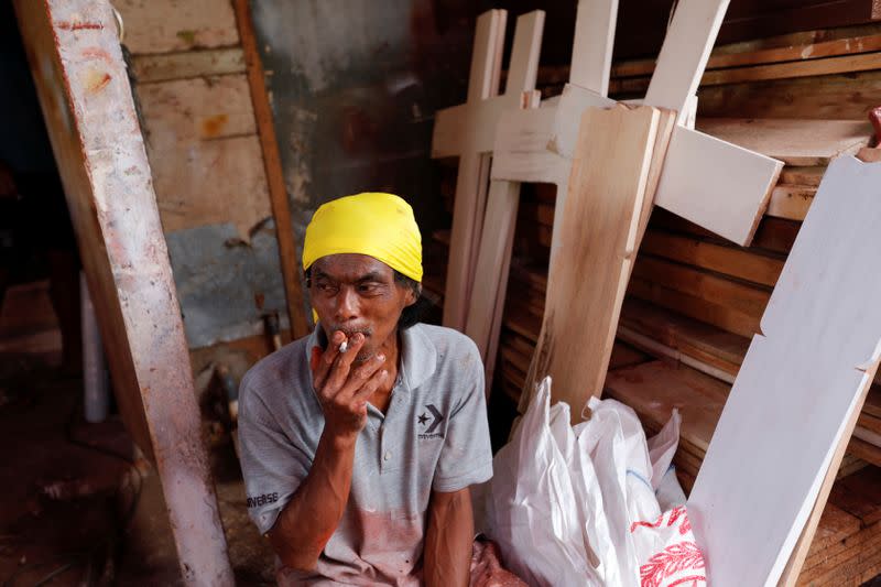 Suherman, a 45-year-old coffin maker, smokes a cigarette while taking a break as he prepares coffins ordered to be donated for the coronavirus disease (COVID-19) victims at a workshop inside a funeral complex in Jakarta