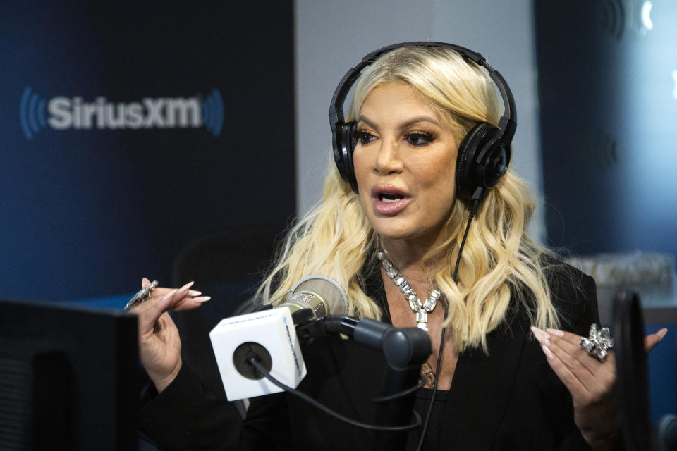 Tori Spelling is wearing headphones and black clothing as she speaks into a microphone during an interview on SiriusXM Radio.