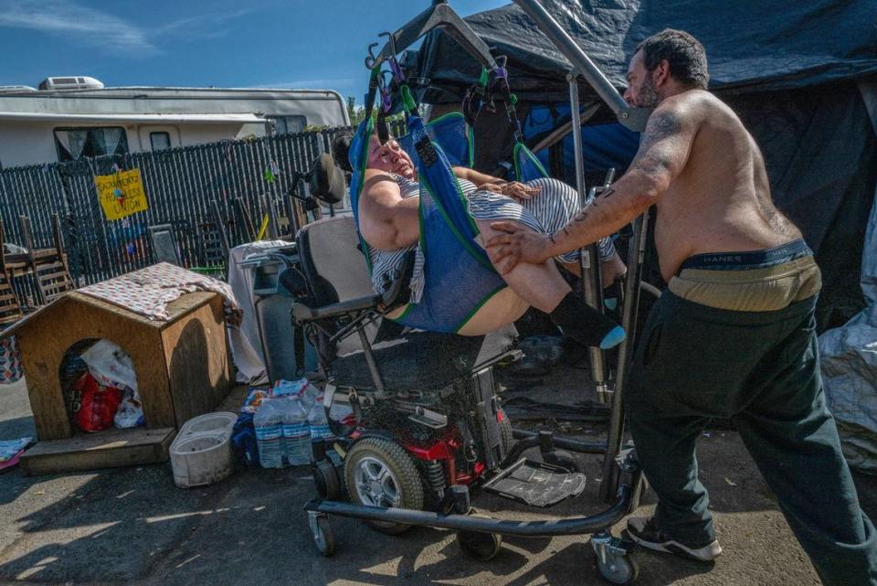 Holly Porter, 40, stops her brother Mike Porter from placing her in a donated wheelchair Friday when the armrest prevented her from sliding into it. Because she couldn’t use the wheelchair, Porter had to sign her housing application while in the hydraulic lift, since the property management representative was not allowed inside her tent for insurance reasons.