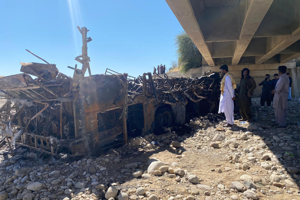 People look at the burnt wreckage of a bus accident in Bela, an area of Lasbela district of Balochistan province, Pakistan, Sunday, Jan. 29, 2023. The passenger bus crashed into a pillar and fell off a bridge, catching fire and killing dozens of people in southern Pakistan on Sunday, a government official said. (AP Photo/Muhammad Saleem)