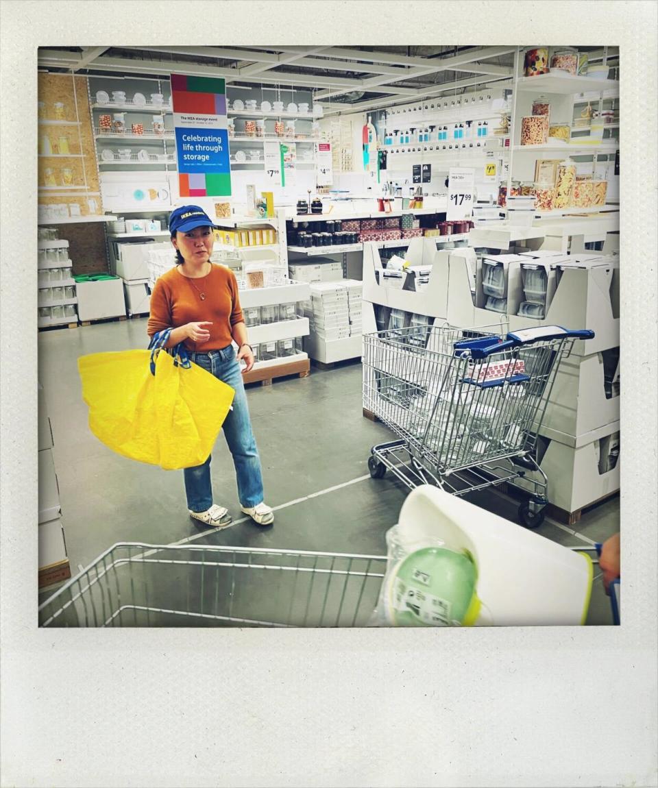 A person wearing a baseball cap carrying a large yellow shopping bag in an Ikea store.