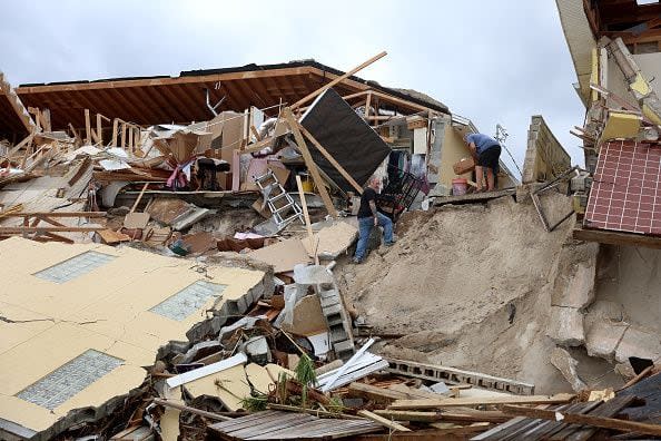 Danny Sonn (left) and Warren Hoganson (right) help homeowner Nina Lavigna salvage what she can from her home after it toppled onto the beach as Hurricane Nicole came ashore on November 10, 2022, in Daytona Beach, Florida. Nicole came ashore as a Category 1 hurricane before weakening to a tropical storm as it moved across the state.