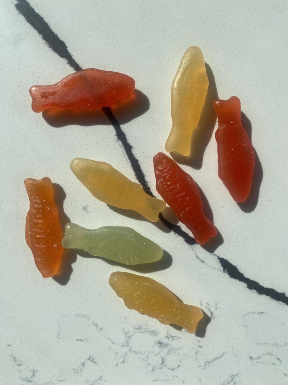 A variety of gummy fish candy scattered on a marble surface