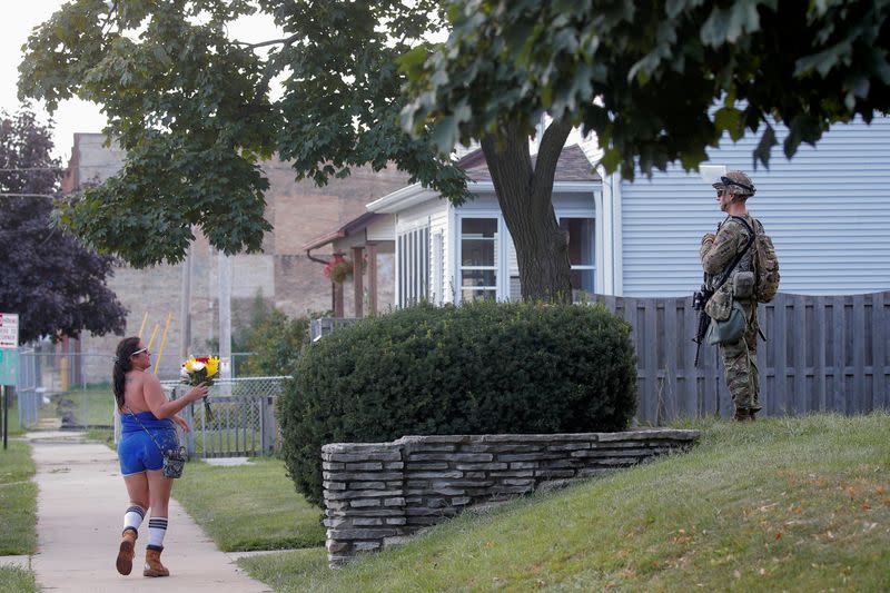 A woman holds flowers near a member of the Wisconsin National Guard standing by as people gather for a vigil, following the police shooting of Jacob Blake, a Black man, in Kenosha, Wisconsin