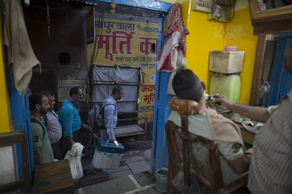 Election officers walk past a barber shop carrying electronic voting machines at the end of polling in Varanasi, India, Sunday, May 19, 2019. Indians voted in the seventh and final phase of national elections, wrapping up a 6-week-long long, grueling campaign season with Prime Minister Narendra Modi's Hindu nationalist party seeking reelection for another five years. Counting of votes is scheduled for May 23. (AP Photo/Rajesh Kumar Singh)