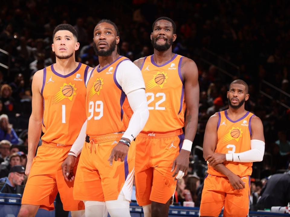 Devin Booker, Jae Crowder, Deandre Ayton, and Chris Paul stand side-by-side and look up during a Suns game.