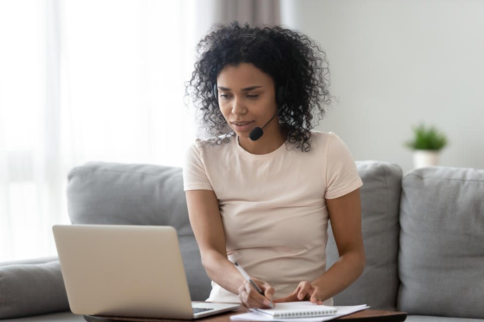 Young african woman wearing wireless headset looking at laptop making notes, focused black girl student teacher watching webinar online training talking by video conference call, e learning concept