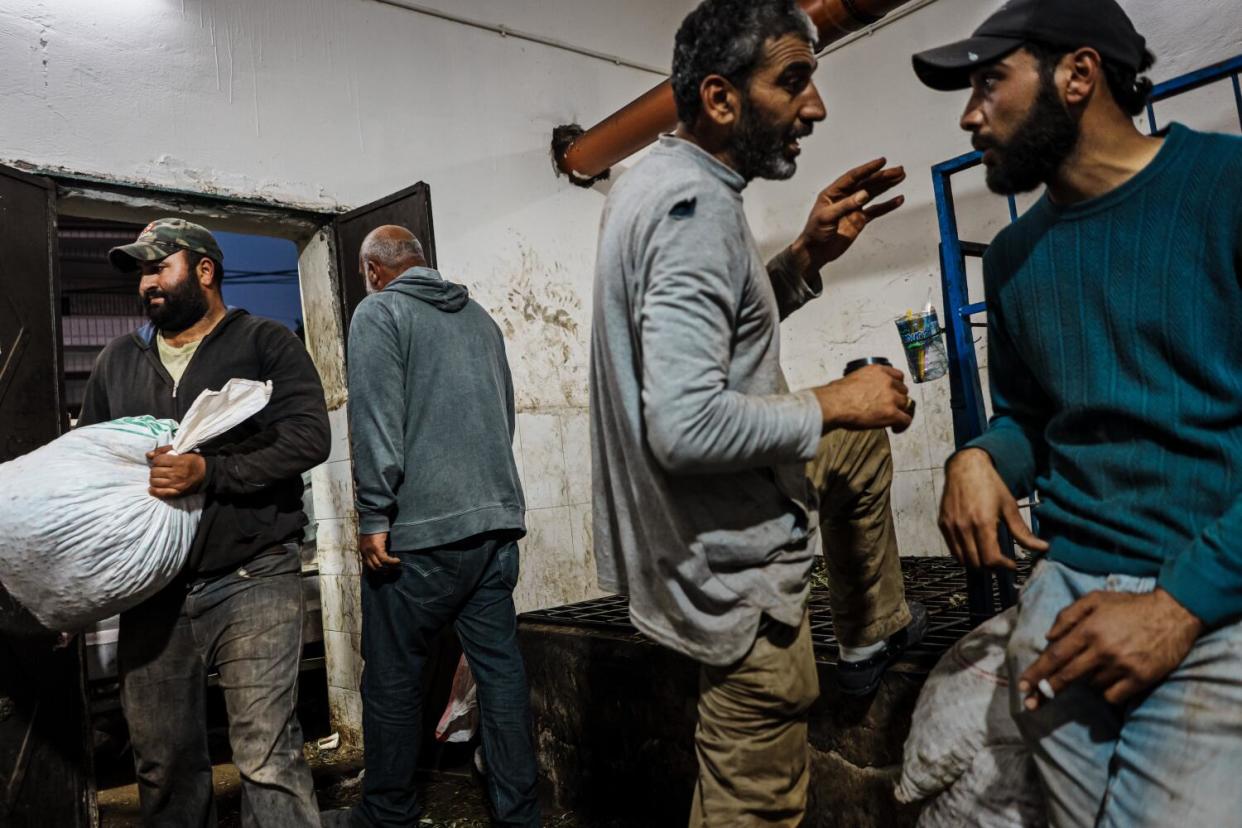 Men talking and working in a grubby factory room, one carrying a full bag