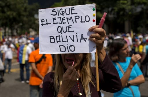 An opposition supporter carries a sign reading "Follow Bolivia's example"