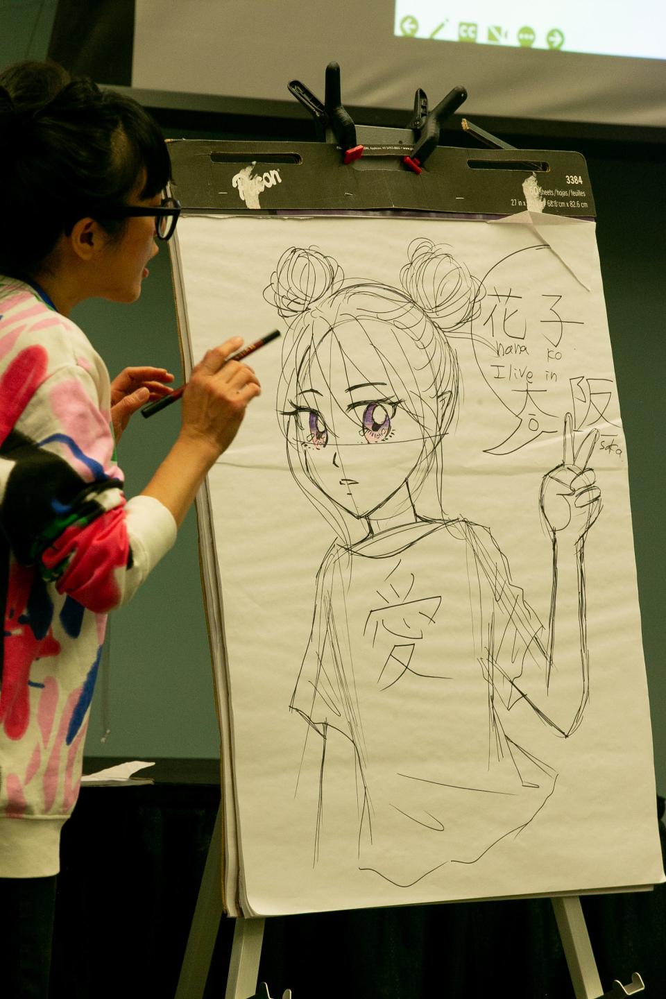 Misako Rocks, a manga writer and illustrator, talks to attendees at a workshop about her finished drawing of a character named Hanako at the 8th Teen Bookfest By the Bay at American Bank Center in Corpus Christi, Texas, Feb. 4, 2023.