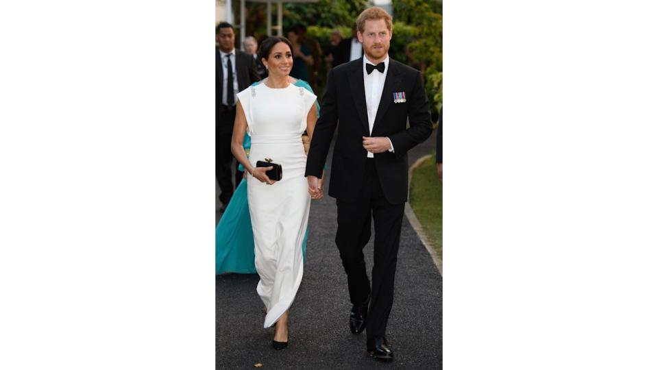 The Duchess of Sussex in a white dress holding hands with Prince Harry