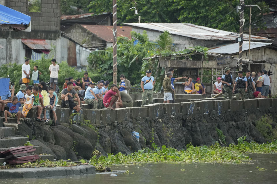 Residents watch rescuers searching for victims of a capsized ferry in Binangonan, Rizal province, Philippines, Friday, July 28, 2023. A boat turned upside down on Thursday when passengers suddenly crowded to one side in panic as fierce winds pummeled the wooden vessel, killing a number of people, officials said Friday. (AP Photo/Aaron Favila)