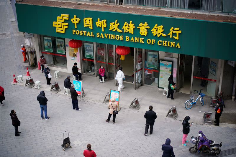 People wearing face masks practise social distancing as they wait outside a Postal Savings Bank of China branch in Wuhan