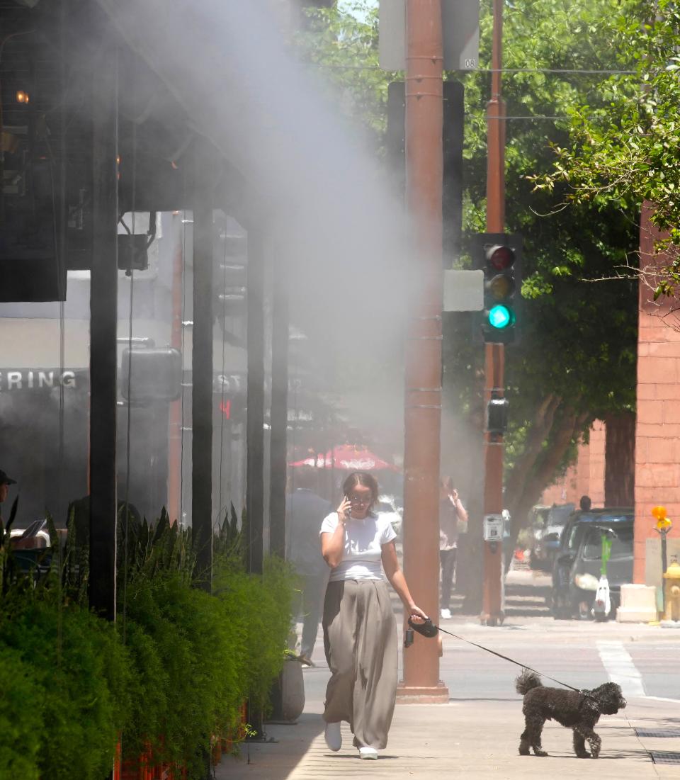 Mary Michael walks her dog Maverick down the sidewalk through a misting system in 108 degree heat on June 6, 2024, in Phoenix, Ariz.