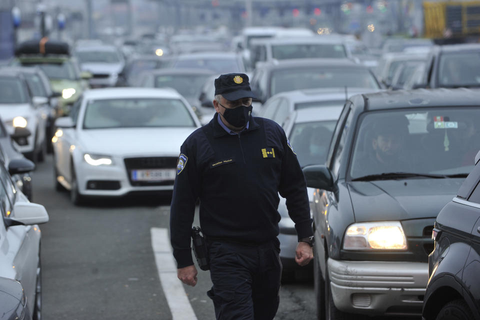 A Croatian border police officer walks between vehicles as motorists wait to cross the Croatian border from Slovenia, at Bregana border crossing, western Croatia, Saturday, Dec. 19, 2020. Balkan citizens going home from Western Europe for holidays have created huge traffic jams at border crossings despite coronavirus restrictions meant to discourage travel for Christmas and the New Year. Huge lines of cars have formed on the borders between Slovenia and Croatia as well as Hungary and Serbia as thousands of people waited for hours Saturday to cross. (AP Photo)