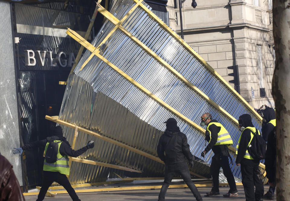 Protesters remove a protective wall from a luxury shop during a yellow vests demonstration Saturday, March 16, 2019 in Paris. Paris police say more than 100 people have been arrested amid rioting in the French capital by yellow vest protesters and clashes with police. They set life-threatening fires, smashed up luxury stores and clashed with police firing tear gas and water cannon (AP Photo/Christophe Ena)