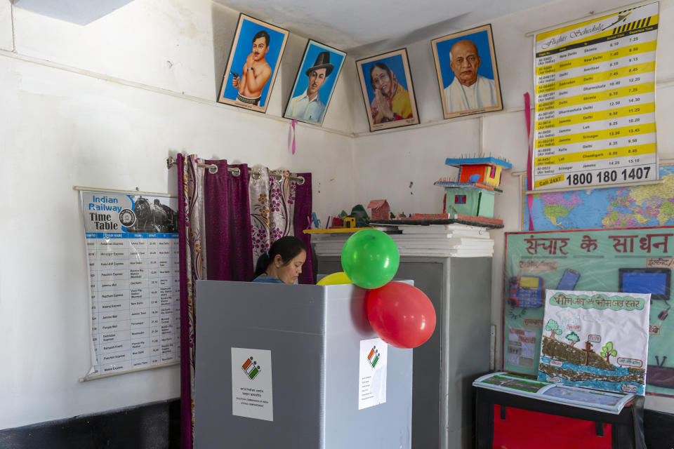 Portraits of Indian political leaders are seen on a wall of a polling booth as a voter casts her ballot in a bypoll for an assembly seat in Dharmsala, India, Monday, Oct. 21, 2019. The seat was vacated by Kishan Kapoor, a Bharatiya Janata Party member of legislative assembly , who was elected to the Lok Sabha in May as Voting is underway in two Indian states of Maharashtra in the west and Haryana in the north where the Hindu nationalist Bharatiya Janata Party (BJP) headed by prime minister Narendra Modi is trying to win a second consecutive term. (AP Photo/Ashwini Bhatia)