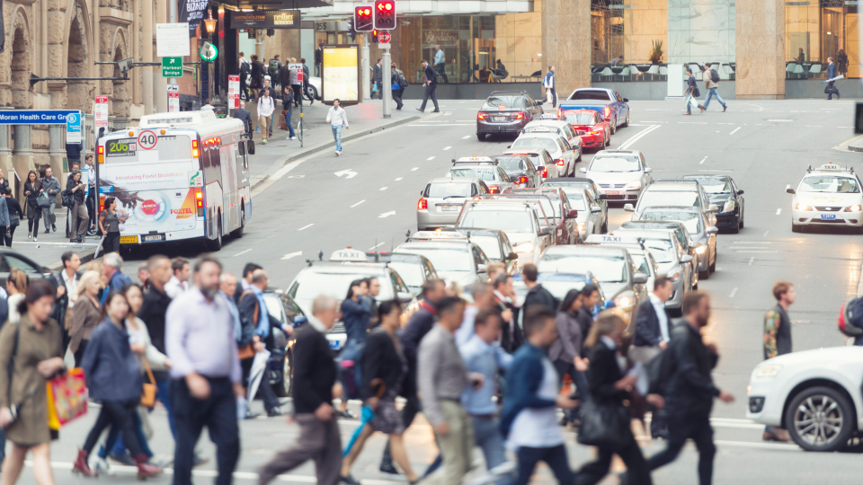 A crowd of people crossing a busy road in a city.