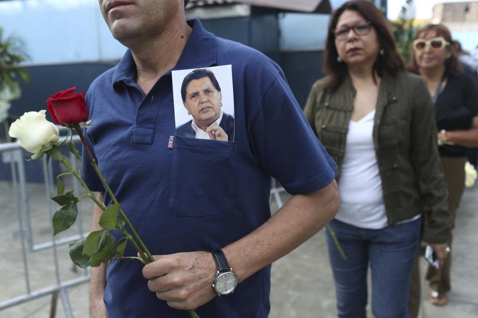 A man wearing a photograph of Peru's late President Alan Garcia arrives to Garcia's political party headquarters where his wake is taking place in Lima, Peru, Friday, April 19, 2019. Garcia shot himself in the head and died Wednesday as officers waited to arrest him in a massive graft probe that has put the country's most prominent politicians behind bars and provoked a reckoning over corruption. (AP Photo/Martin Mejia)