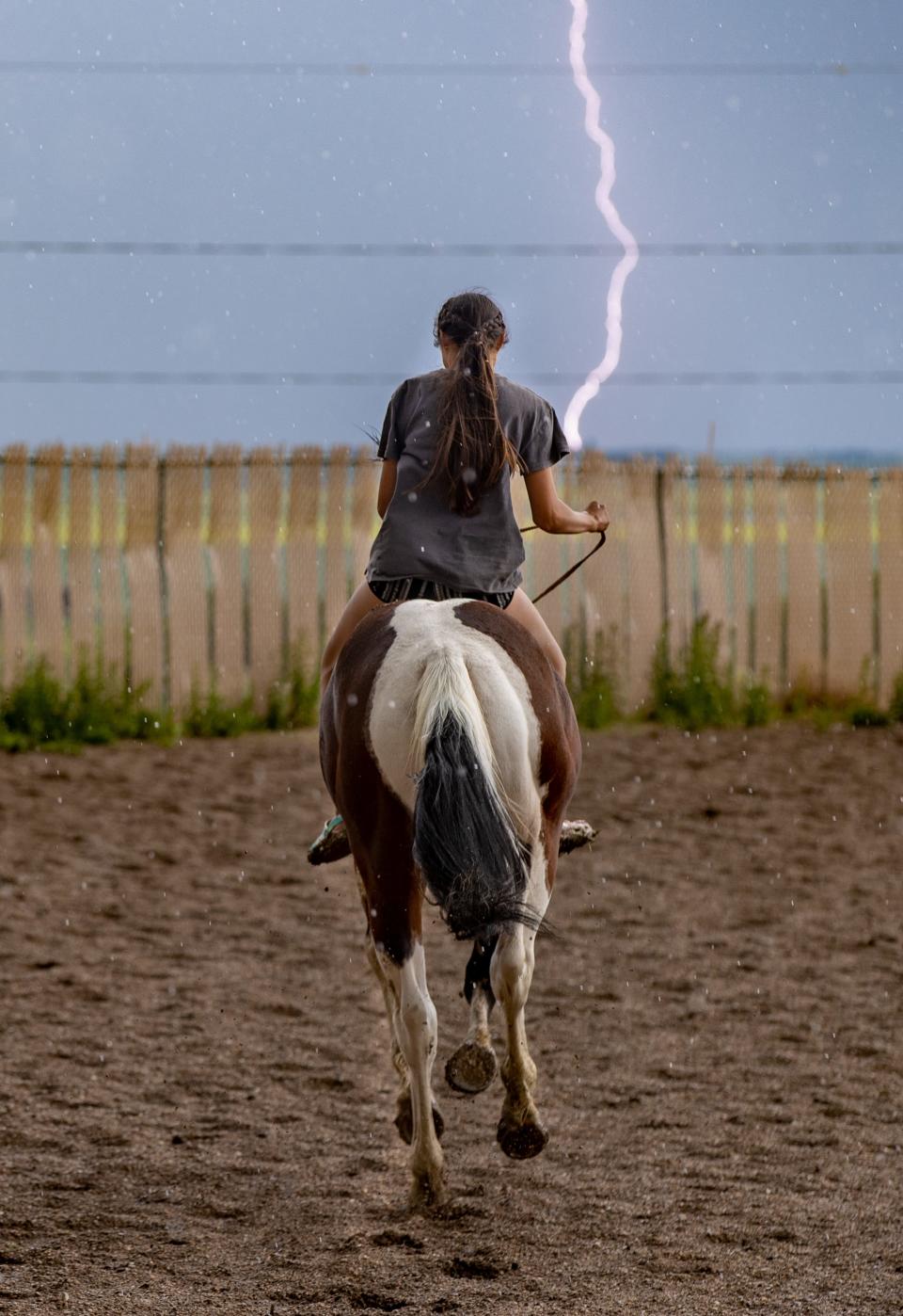 Lightning strikes in the distance as a young rider takes off on a horse at the Parshall Lucky-Mound Rodeo in North Dakota.