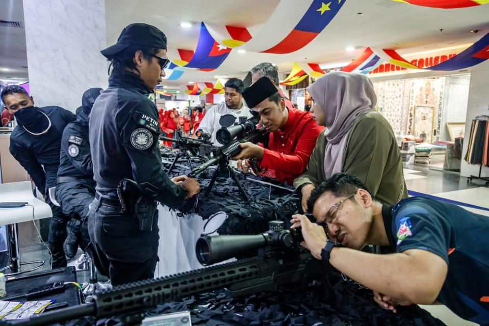 Visitors take pictures with semi-automatic and automatic weapons at the Mindef booth during the 2024 Umno General Assembly in Kuala Lumpur on August 23, 2024. — Photo by Firdaus Latif