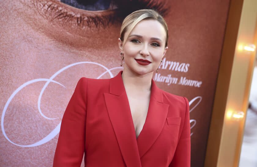 A woman with blond hair pulled back into a bun posing in a red suit and red lipstick