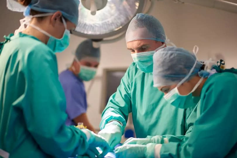 A female operating nurse stands over a patient at the operating table