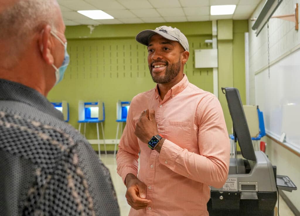 Mandela Barnes speaks with Gary Sprong as he places an “I Voted” sticker on his chest Tuesday, Aug. 9, 2022, during the partisan primary at Green Tree Preparatory Academy located at 6850 N. 53rd St., Milwaukee. Barnes is the democratic candidate running for U.S. Senate. (Ebony Cox/Milwaukee Journal-Sentinel via AP)