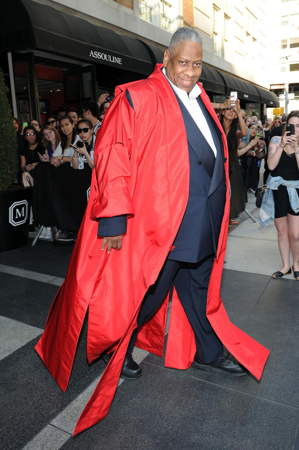 Andre smiles as he stands in front of a building wearing one of his iconic coats