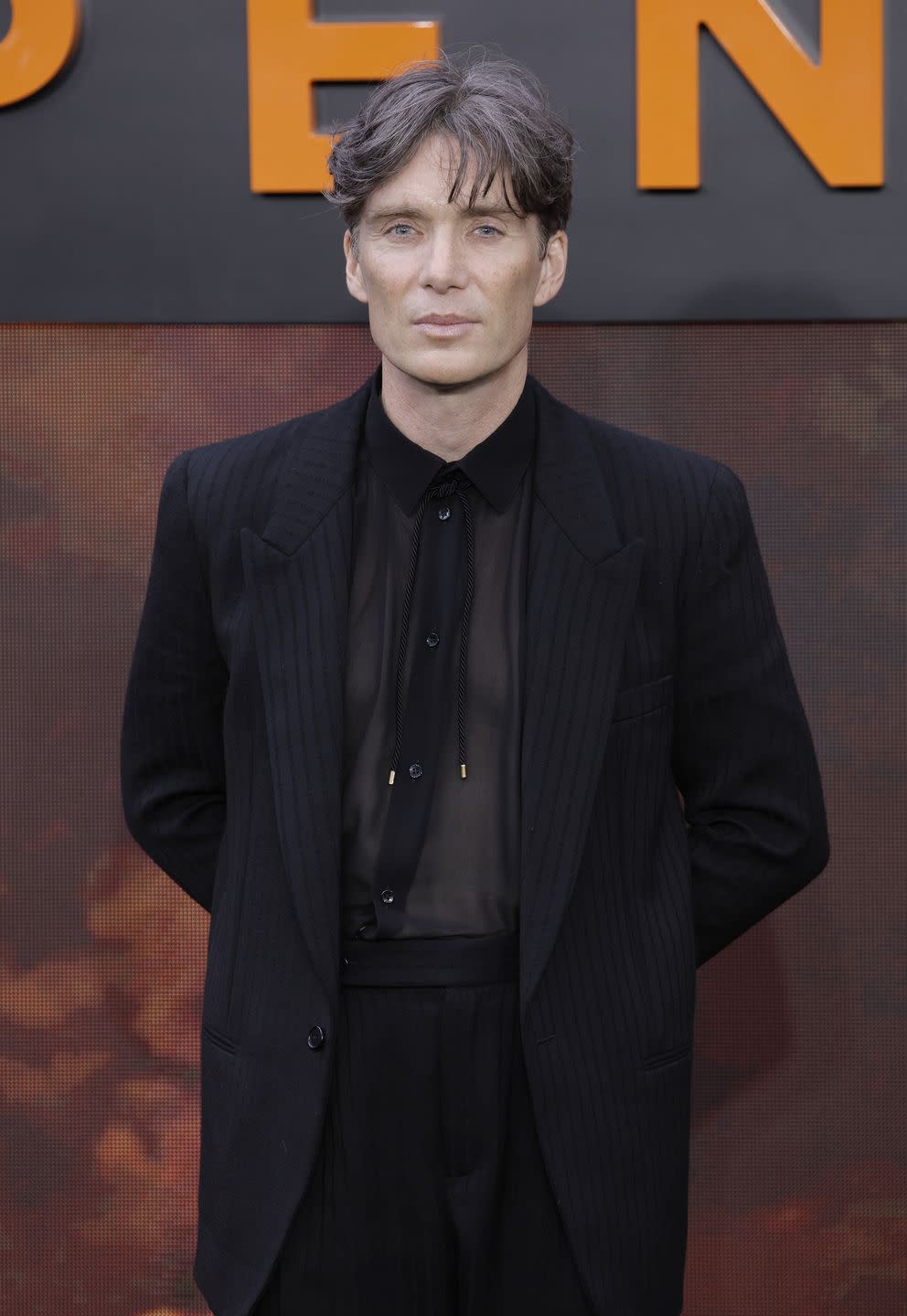 cillian murphy poses for the camera in a black suit and black shirt