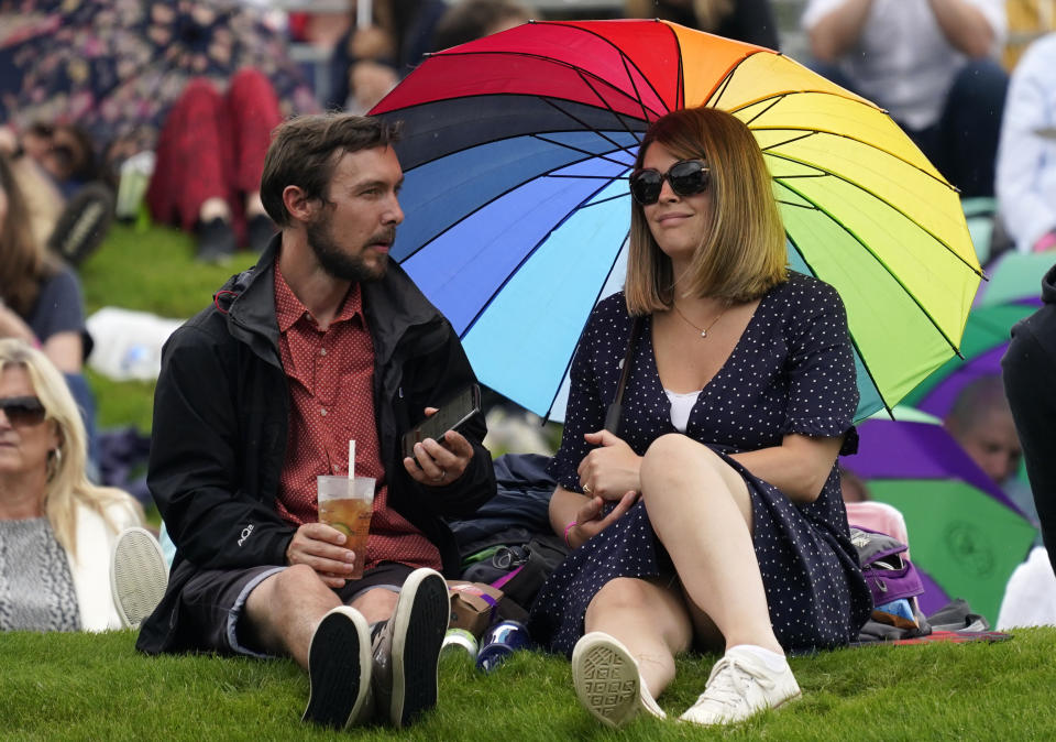 People shelter under an umbrella during a rain delay on day one of the Wimbledon Tennis Championships in London, Monday June 28, 2021. (AP Photo/Alberto Pezzali)