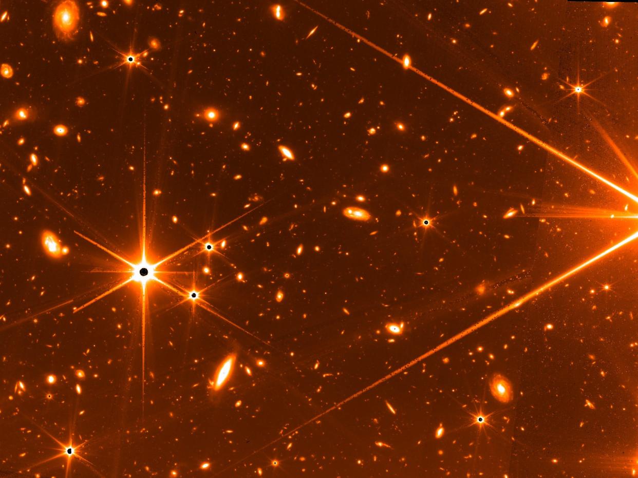 orange image of deep space from the infrared james webb space telescope with galaxies and black stars with long orange rays
