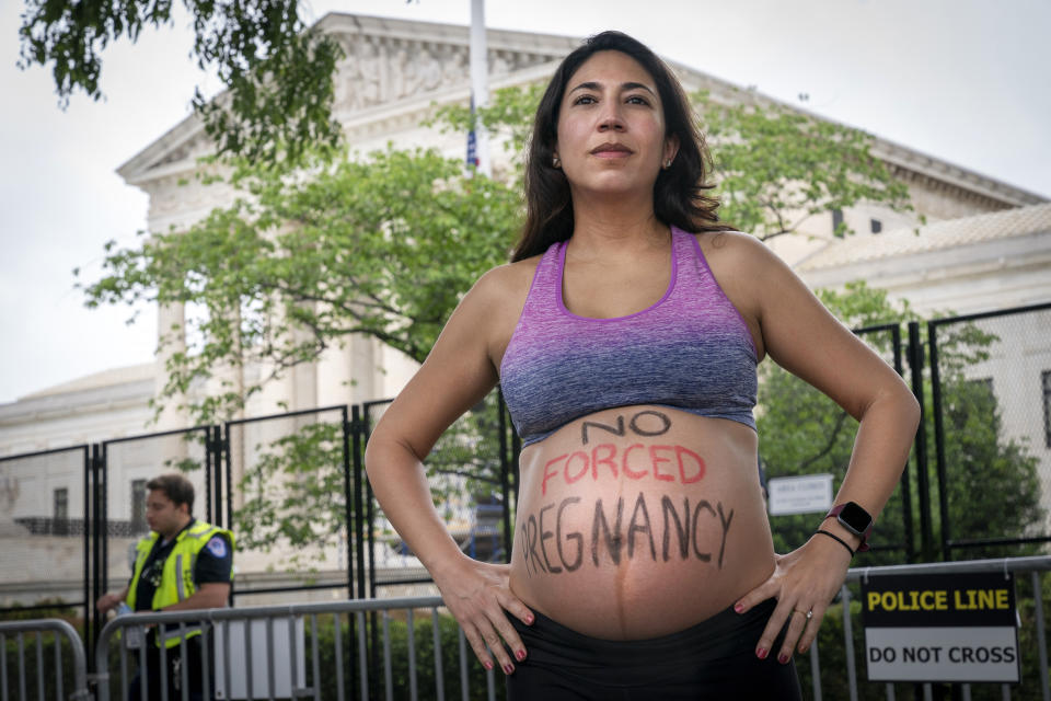 Julia Bradley-Cook, of Washington, who is 7 months pregnant, poses for a portrait as she protests for abortion rights, Saturday, May 14, 2022, outside the Supreme Court in Washington, during protests across the country. "I think there is a dichotomy set up on abortion and pregnancy," says Bradley-Cook, "it's important to show that just because we support the right to choose, doesn't mean we can't also be pregnant." On her belly she has written, "no forced pregnancy." (AP Photo/Jacquelyn Martin)
