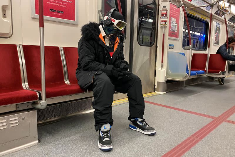 A man wearing ski goggles, gloves and clothing rides the subway during the global outbreak of coronavirus disease in Toronto