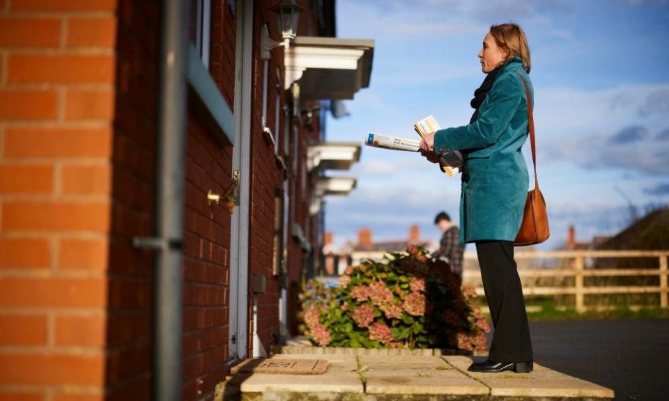 Helen Morgan viewed from side on, standing on a doorstep holding election literature