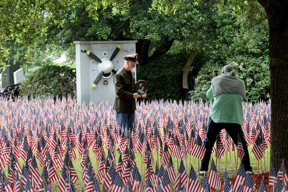 A man holds an old portrait as he poses for a photo among some of the 26,000 flags placed in the garden at the National Museum of the Mighty 8th Air Force on Friday, May 26, 2023 following the opening ceremony for the 3rd annual Flags for the Fallen. 