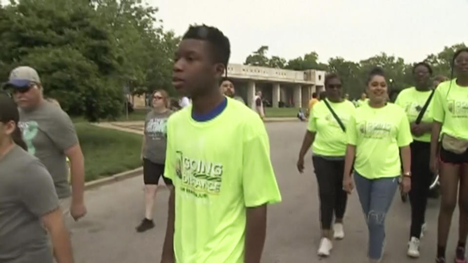 In this image made from video provided by KCTV, Ralph Yarl, center, wearing a bright green "Team Ralph" shirt, participates in a walk in an event called "Going the Distance for Brain Injury" at Loose Park in Kansas City, Mo., Monday, May 29, 2023. Yarl, a Black teenager who was shot in the head and arm in April after mistakenly ringing the wrong doorbell, walked at the brain injury awareness event Monday in his first major public appearance since the shooting. (KCTV via AP)