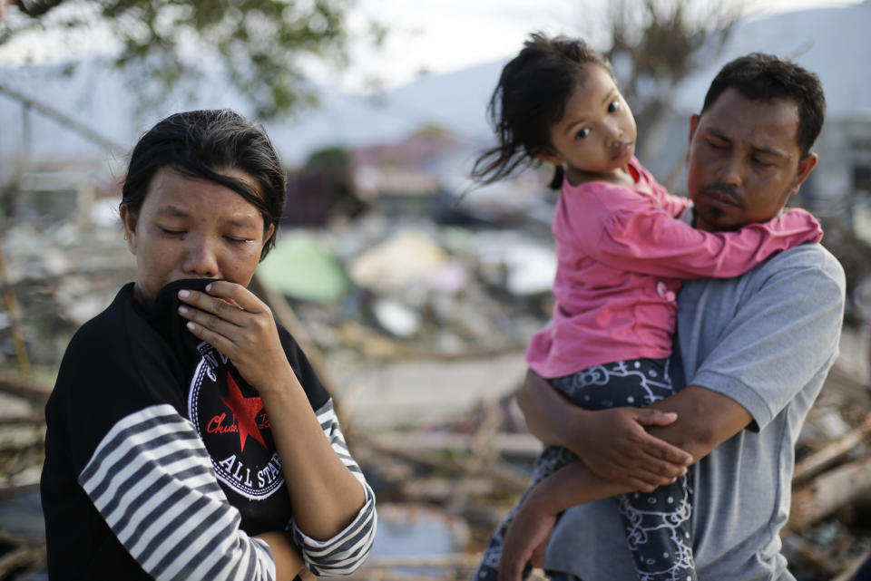 In this Oct. 5, 2018, photo, Musrifah, left, cries beside her husband Hakim and daughter Syafa Ramadi as they visit the area where their house used to stand before a massive earthquake and tsunami hit their seaside village in Palu, Central Sulawesi, Indonesia. The family lost their son. The 7.5 magnitude quake triggered not just a tsunami that leveled huge swathes of the region's coast, but a geological phenomenon known as liquefaction, making the soil move like liquid and swallowing entire neighborhoods. (AP Photo/Aaron Favila)