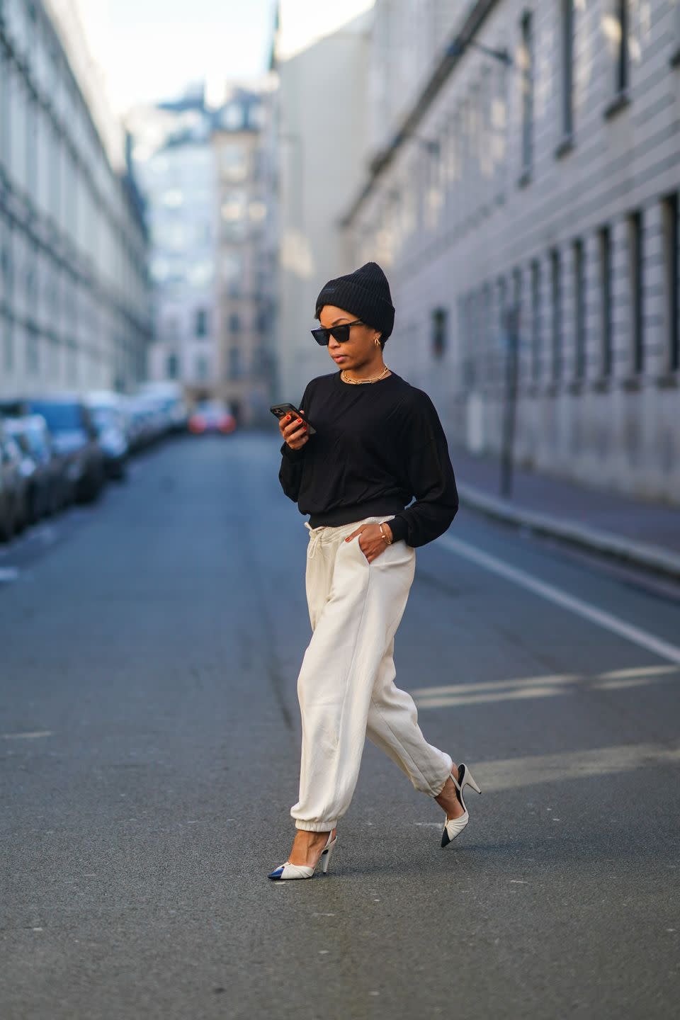 paris, france february 11 ellie delphine wears a beanie hat, sunglasses, golden earrings, a golden chain necklace, a black pullover from hm, white jogger sport pants from hm, high heels pointy shoes from saint laurent ysl, on february 11, 2021 in paris, france photo by edward berthelotgetty images