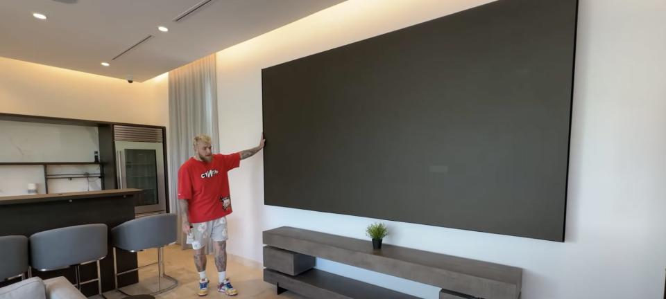 Jake Paul standing beside a large TV.