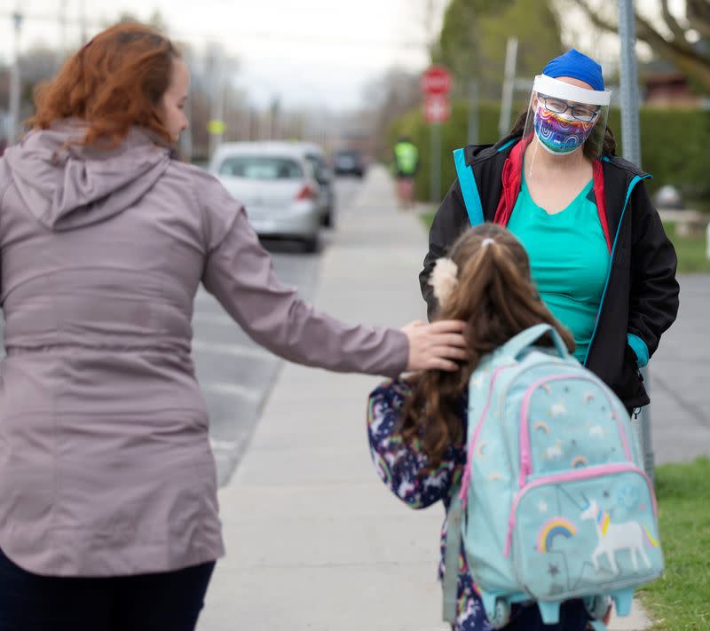 A teacher greets a student and her mother as schools reopen outside the greater Montreal region in Saint-Jean-sur-Richelieu