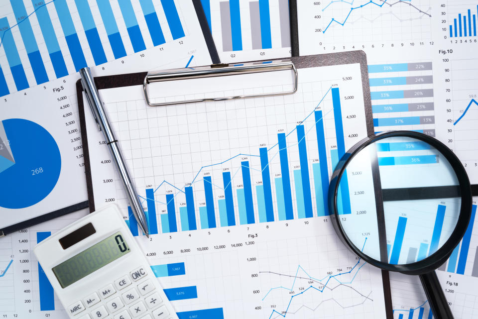 A calculator, pen, and magnifying glass on top of multiple financial charts